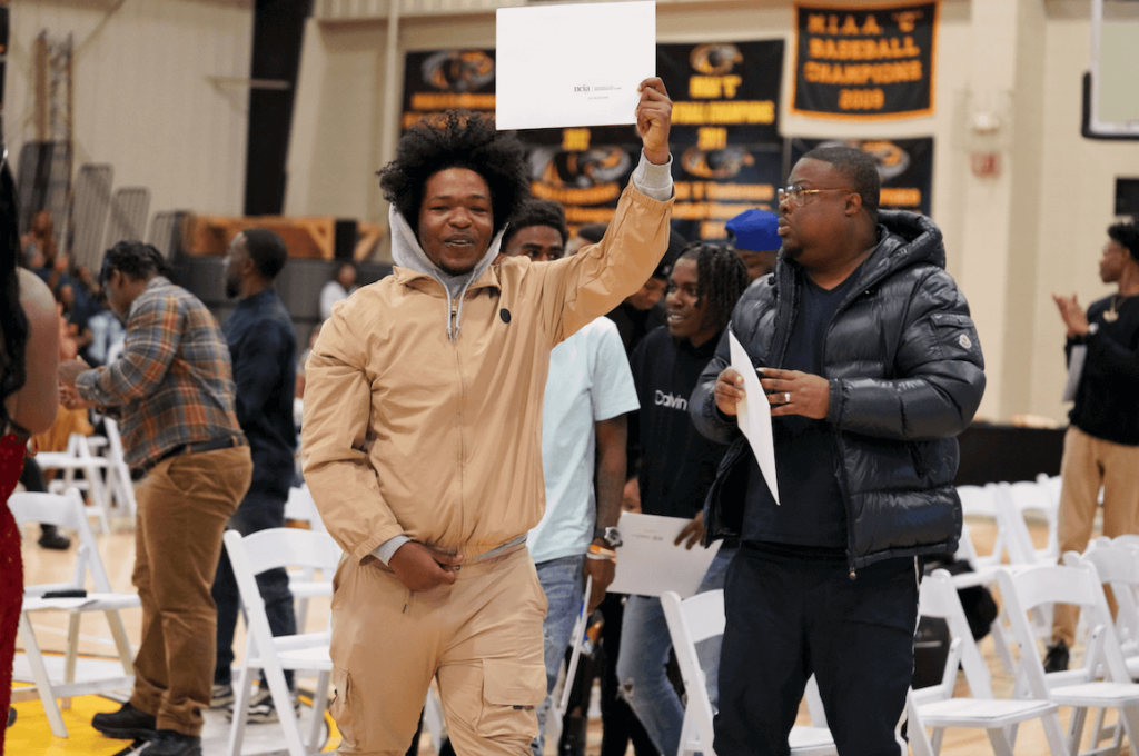 image of a graduate of the VTC holding up his certificate walking down the aisle